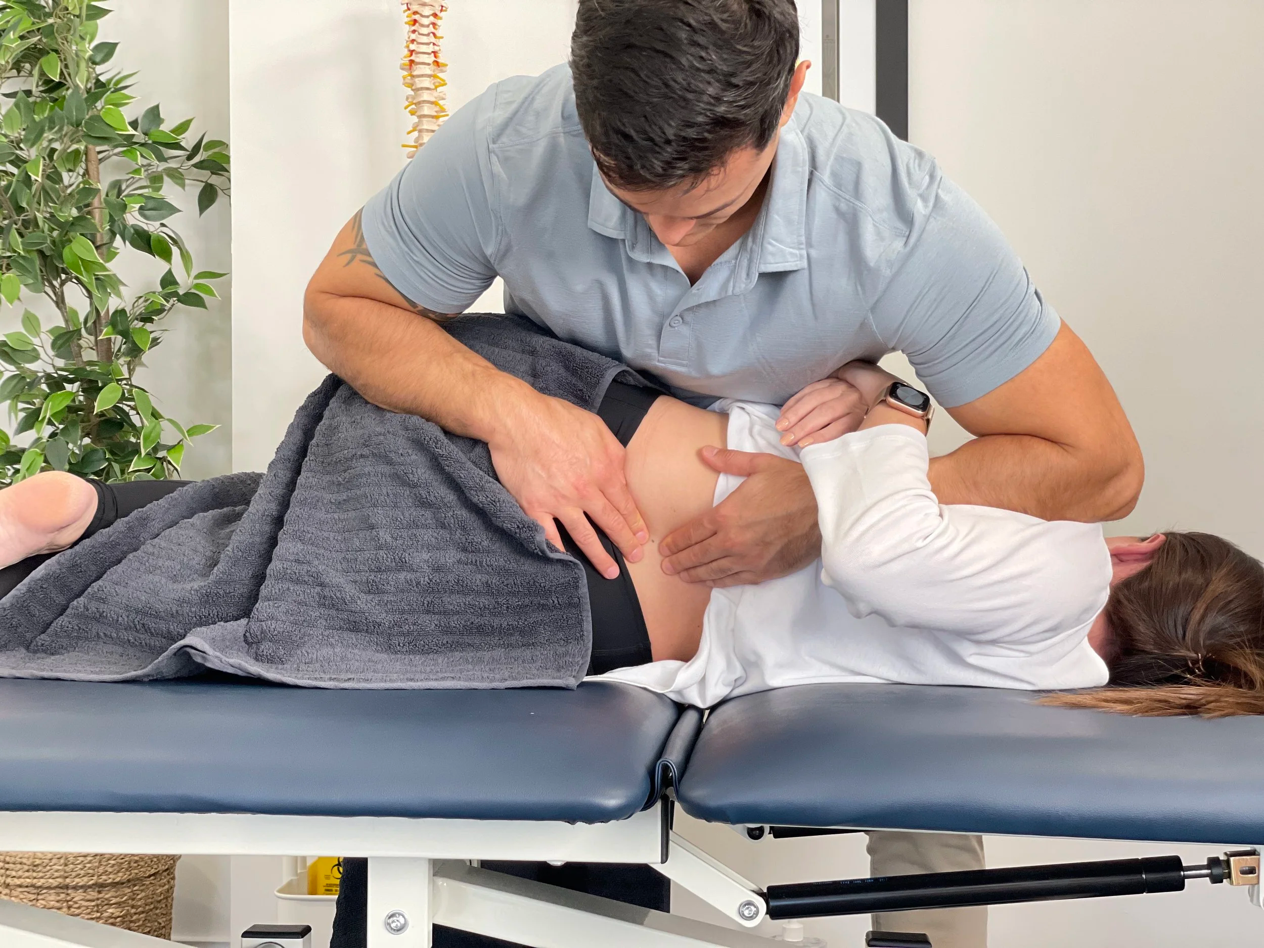 A physiotherapist performing a hands-on lower back technique on a patient at the clinic.